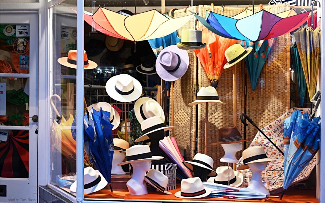 Panama hats and umbrellas in Aug 2025 display window of T Snook, hat shop in Bridport, Dorset, UK